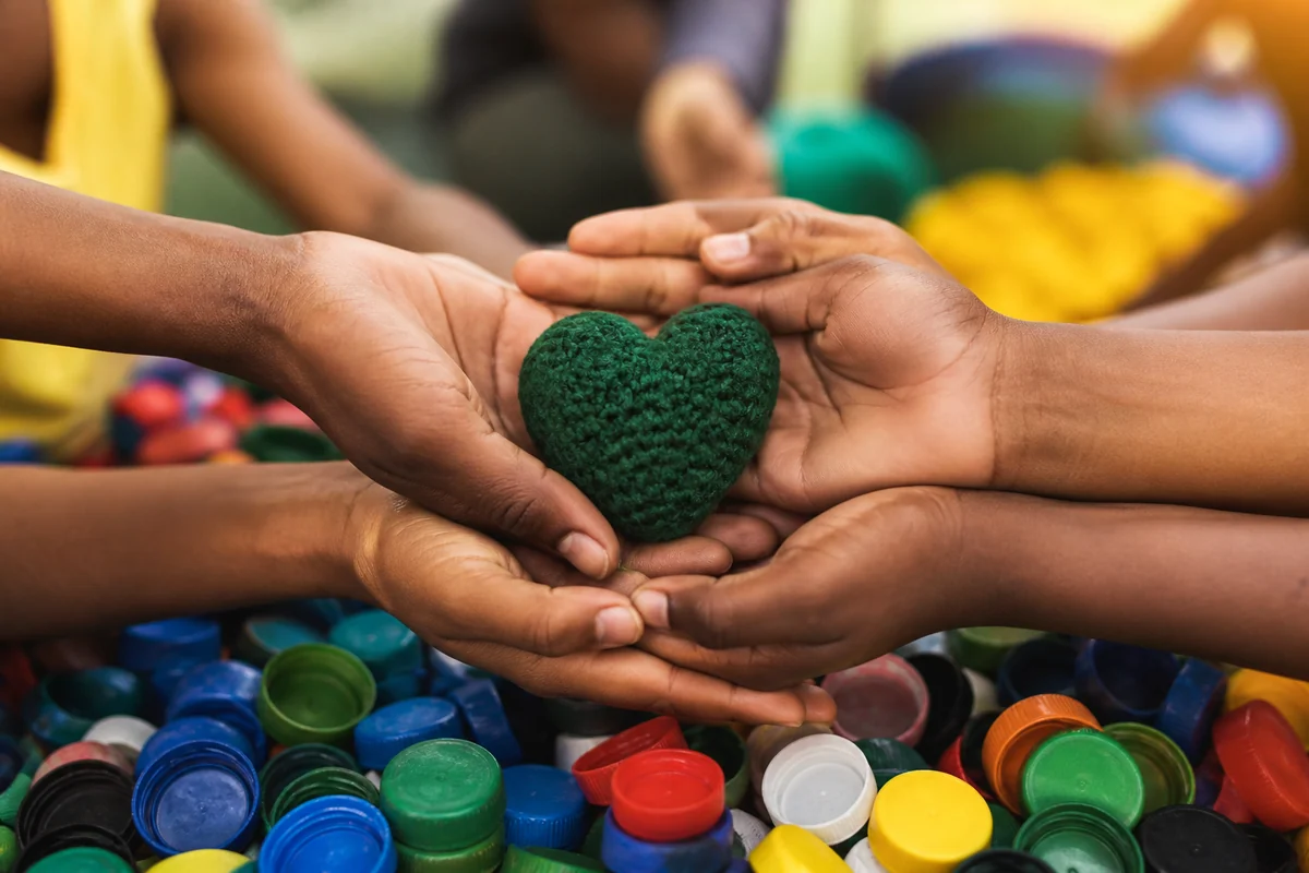 Mãos reunidas segurando um coração verde sobre tampinhas coloridas